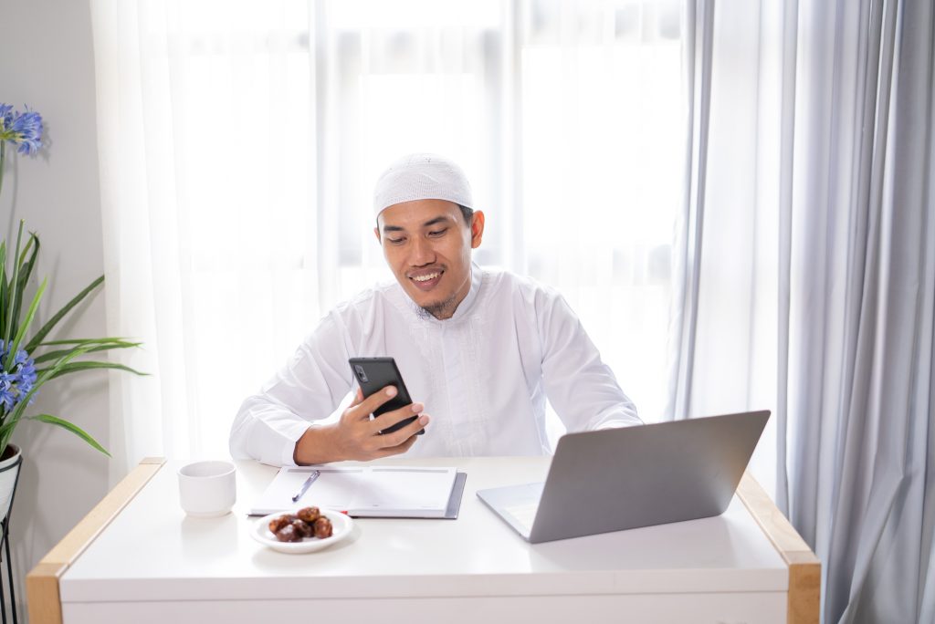 Muslim businessman using his smartphone and laptop working from home